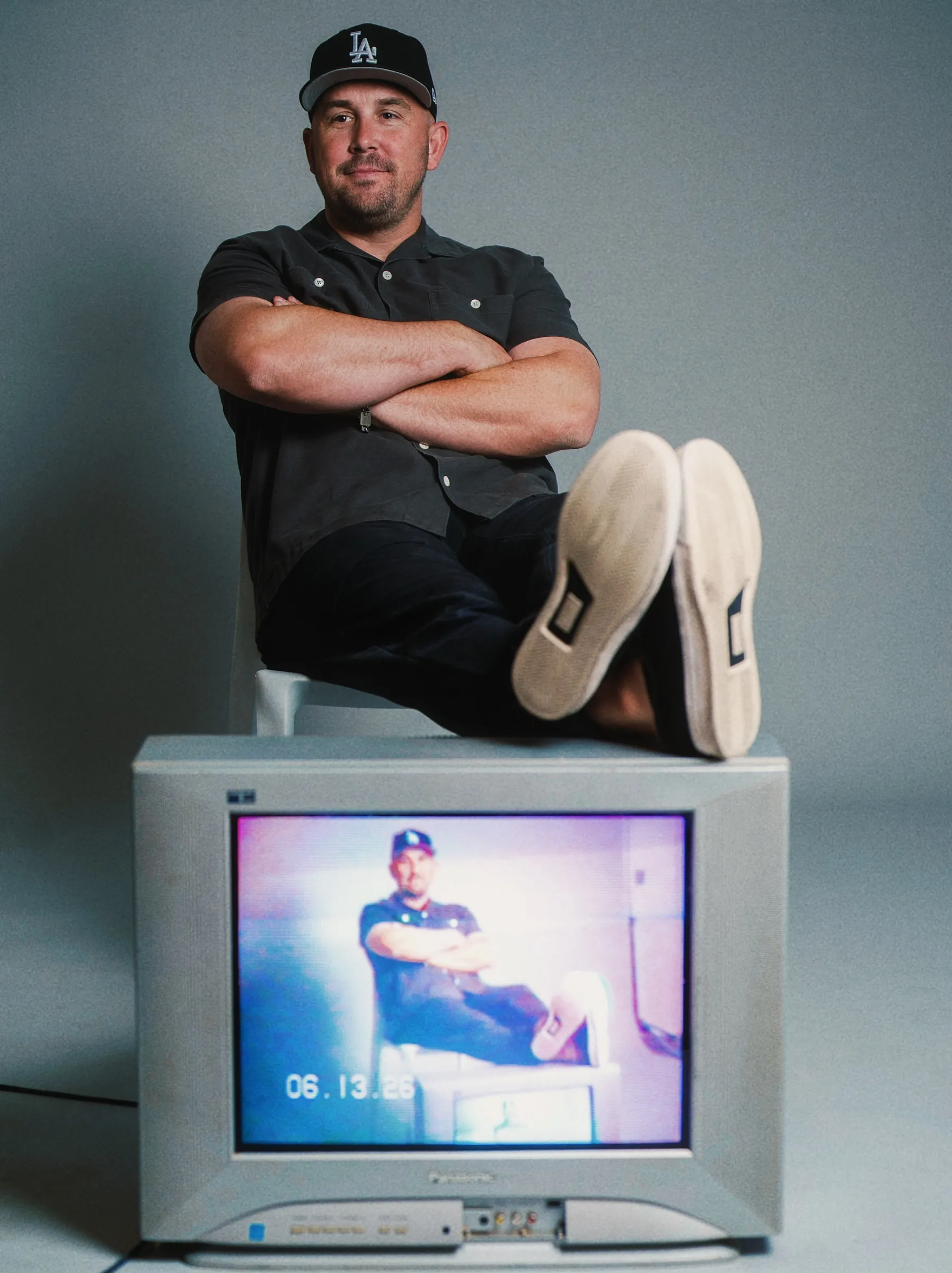 Tyler Cherman seated on a vintage CRT monitor showing the same shot with burned-in timecode.